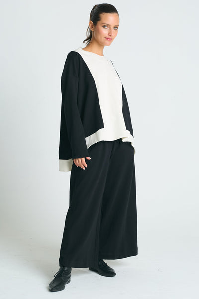 A woman wearing a color block sweatshirt with black and white sections, paired with wide-leg pants and black shoes.
