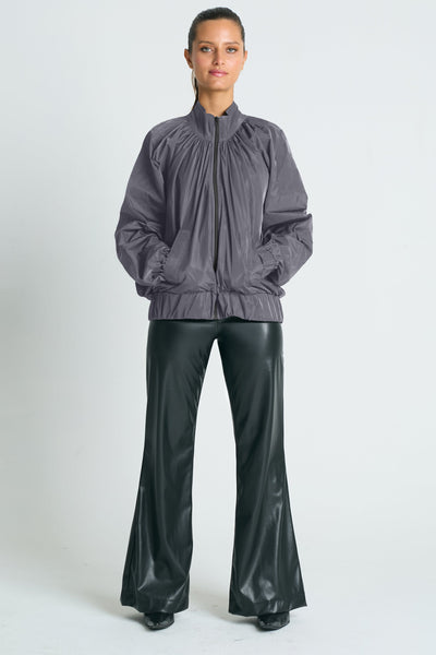 A model wearing a gray nylon bomber jacket with ruched details and a gathered neckline, paired with black wide-leg pants.