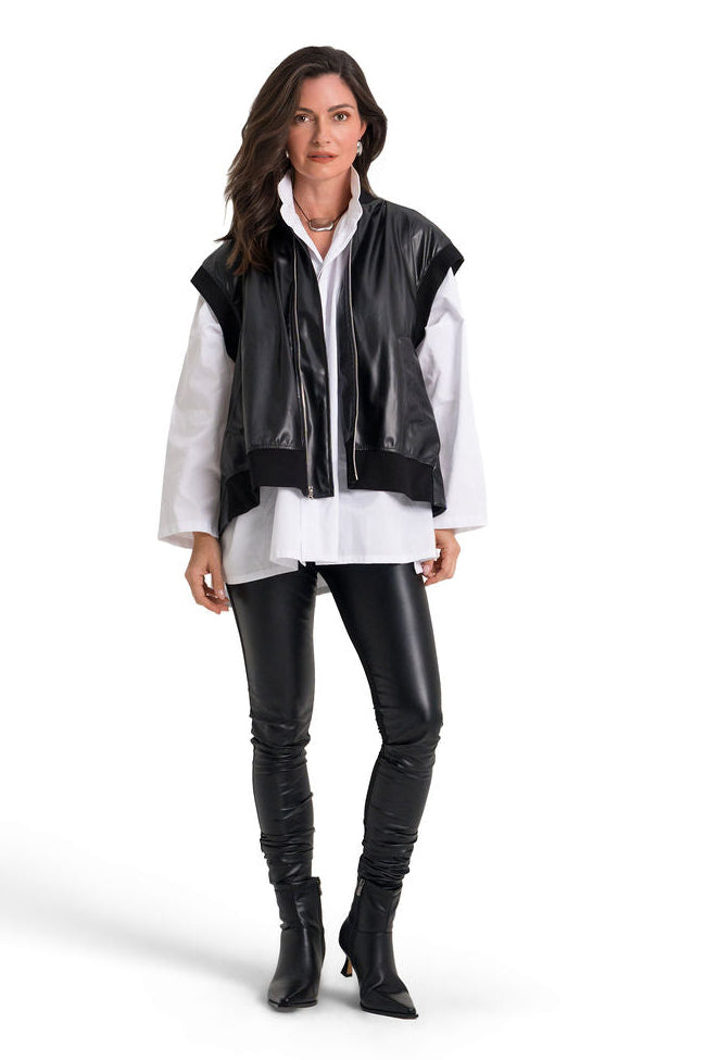 A woman modeling a black faux-leather vest over a white button-up shirt, paired with black faux-leather pants and black ankle boots, on a solid white background.