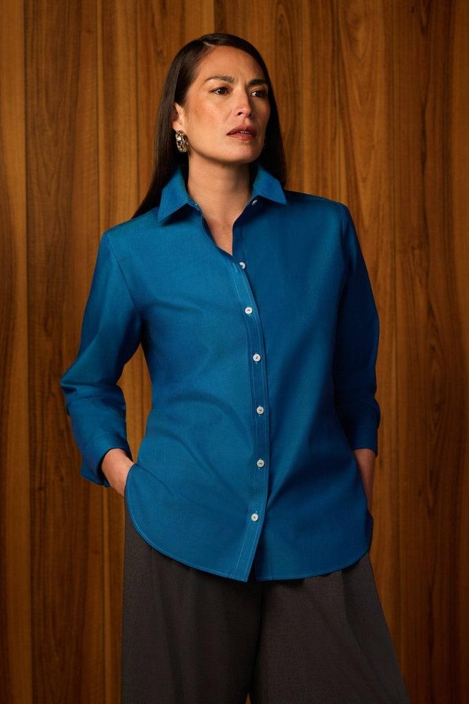 Women with hands on her hips wearing the Meghan No Iron Pinpoint Long Sleeve Shirt with a wooden background #color_teal