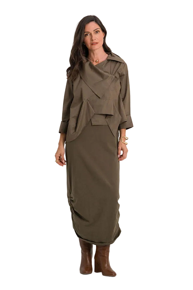 A woman modeling a matching 100% cotton two-piece olive green outfit consisting of a draped long-sleeve top and a matching midi skirt, paired with brown leather boots, against a plain white studio background.