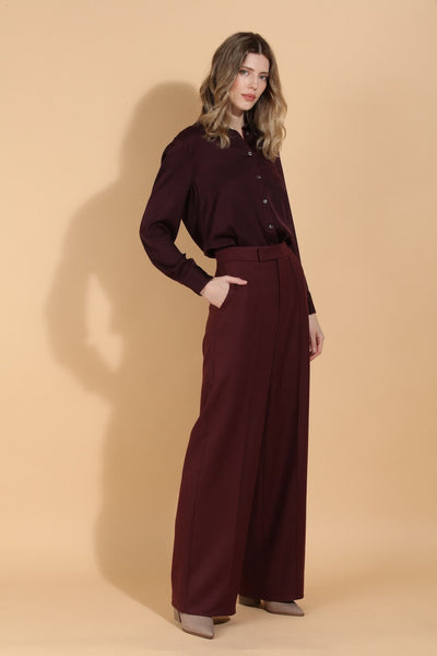 Woman wearing a burgundy shirt and wide-leg pants on a beige background