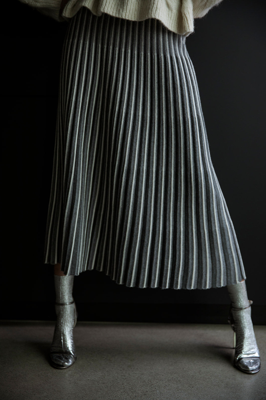 Full-length view of the Adeline Skirt swaying gracefully, showcasing its pleated design and contrasting stripes in motion against a black backdrop.