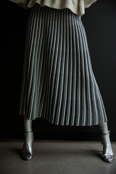 Full-length view of the Adeline Skirt swaying gracefully, showcasing its pleated design and contrasting stripes in motion against a black backdrop.