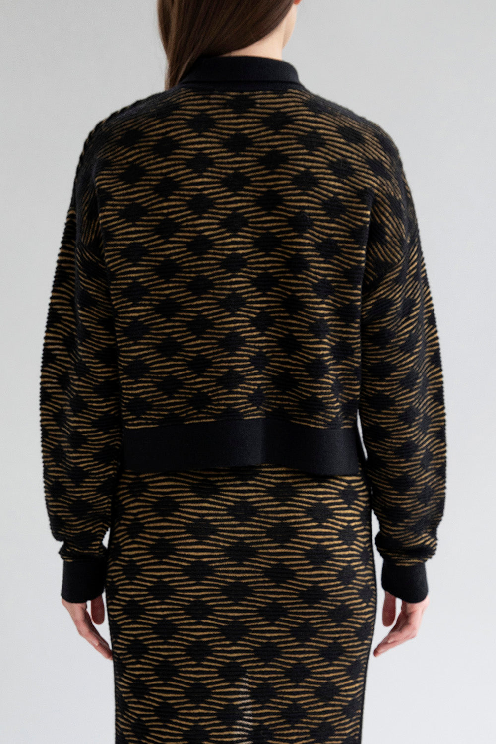 Full back view of a model wearing the Amelie Polo sweater in golden black.