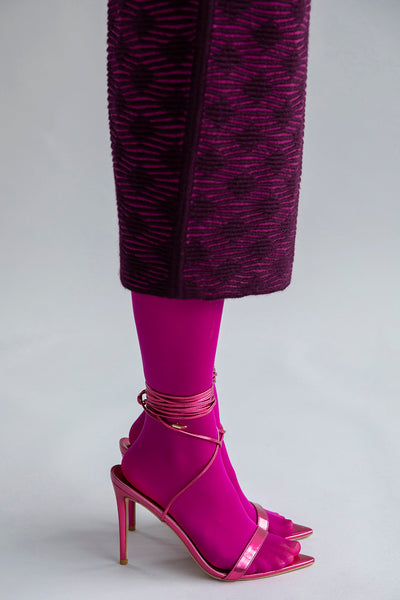 Detail shot of the textured pattern on the fuchsia aubergine Ines skirt, styled with bright pink sheer tights and laced-up high heels.