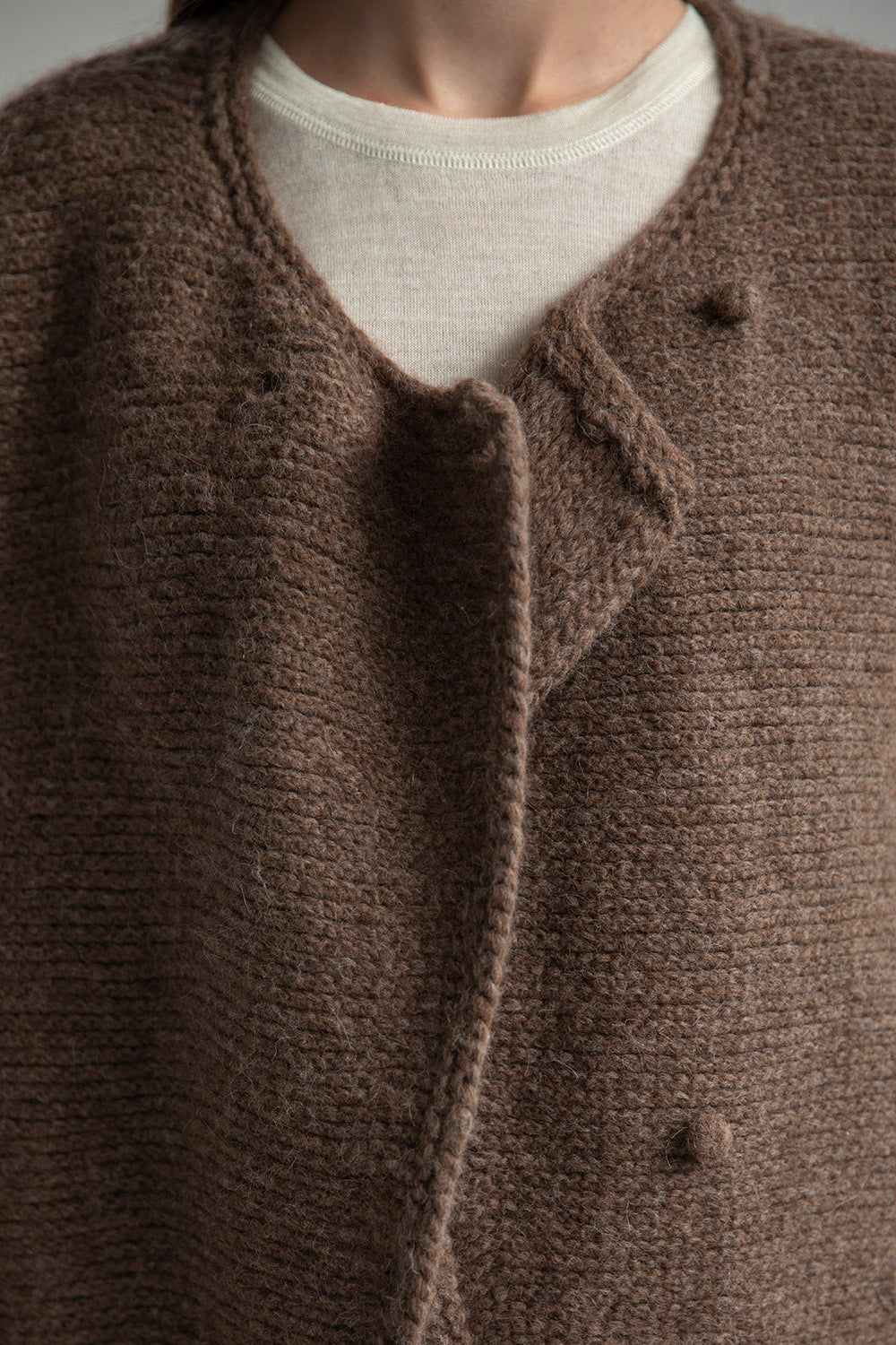 Close-up of the front of the Momo Handknit Cardigan in Saddle, showing the hand-crocheted buttons made from matching yarn. Made from 70% Baby Alpaca 23% Nylon and 7% Merino Wool.
