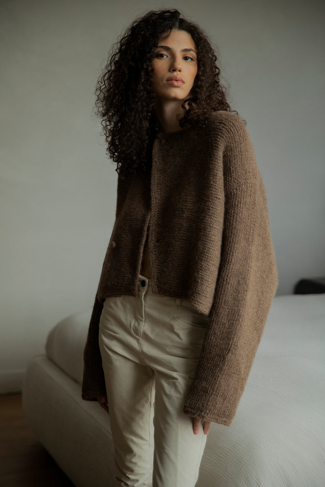 Model looking into mirror, wearing the Momo Handknit in Saddle, a versatile piece ethically made in Peru. Can also be worn upside down for a draped neck.
