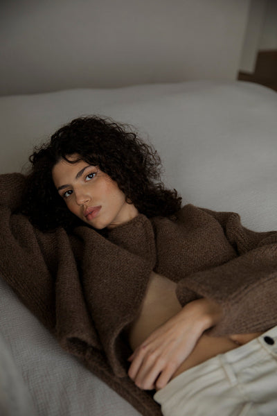 Model Bella wearing the Momo Handknit Cardigan in Saddle, with only the top button fastened. The hand-crocheted button is made from matching yarn, adding a subtle, artisanal touch to the relaxed, cropped fit and textured stitch of the cardigan.