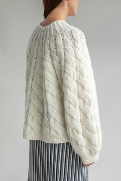 Side view of the Tomo Mix Cable Handknit made with a lightweight alpaca blend yarn. The pullover shows a comfortable fit with ribbed detailing at the cuffs and hem.