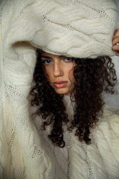 Model Bella peeking through the sleeve of the Tomo Handknit in Ivory, showcasing the dramatic, fluffy texture of the hand-knit design. The soft alpaca blend yarn creates a voluminous, cozy look, emphasizing the warmth and a luxurious feel.