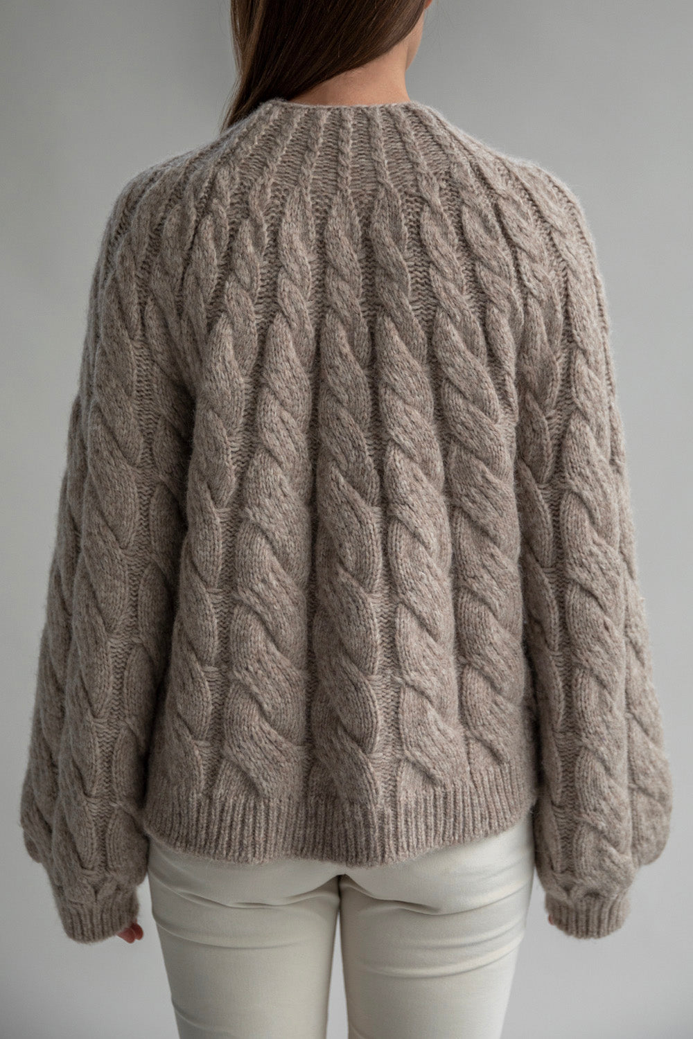 Back view of the Tomo Mix Cable Handknit in Oat Heather showcasing its simple design and soft fabric made from an alpaca blend yarn. The pullover has a relaxed fit and ribbed hems.